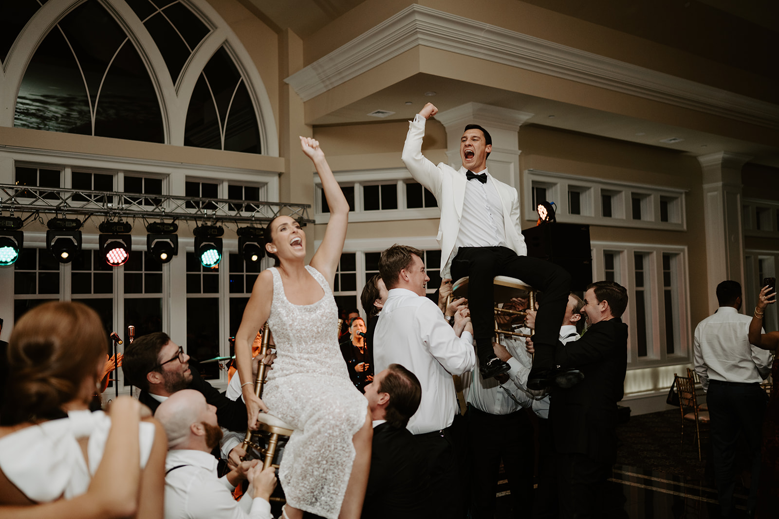 Newlyweds lifted in chairs during the Hora dance, cheering with raised fists as guests celebrate around them.